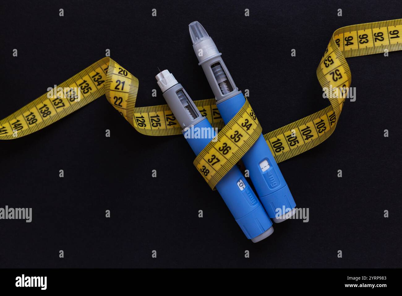 Deux stylos d'injection de drogues ozempic pour la perte de poids avec un ruban à mesurer jaune sur fond noir. Médecine pour diabétiques et perte de poids Banque D'Images
