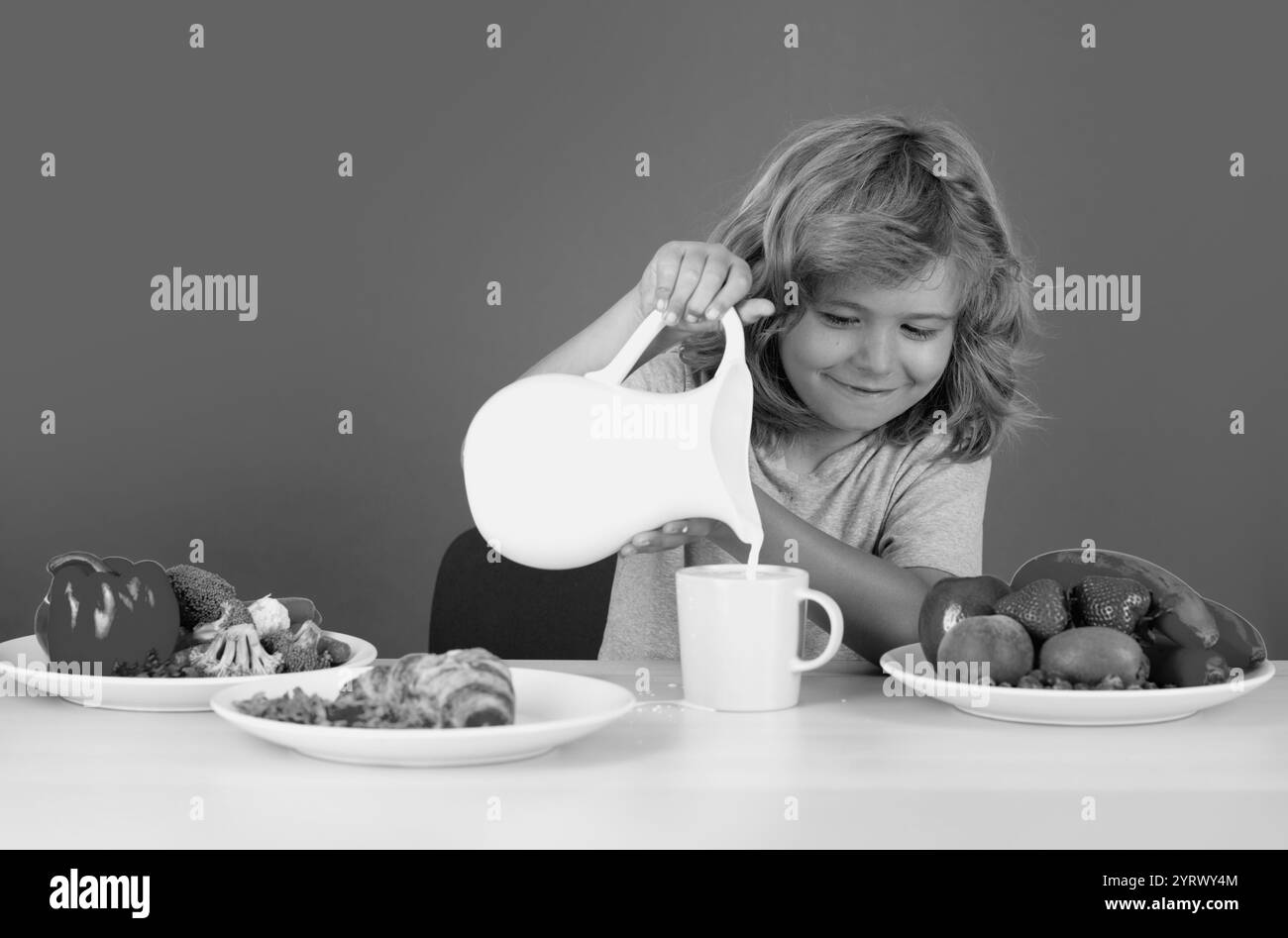 Kid Boy versant du lait de vache entier. Portrait de l'enfant manger des aliments sains frais dans la cuisine à la maison. Petit garçon mangeant le petit déjeuner avant l'école. Enfant en bonne santé po Banque D'Images