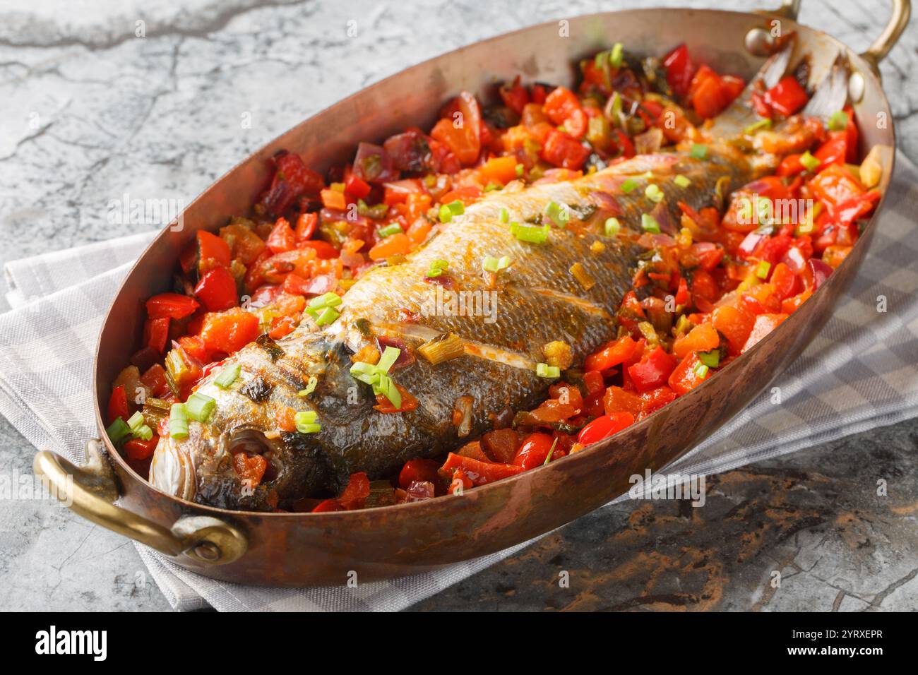 Bar entier cuit avec des légumes de saison tels que le poivre, la tomate, l'oignon, le céleri et l'ail gros plan dans une poêle sur la table. Horizontal Banque D'Images