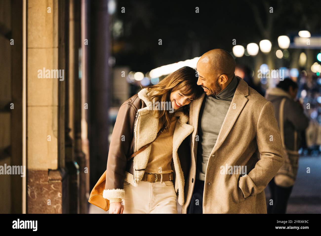 Un couple aimant partage un moment joyeux tout en se promenant dans une rue de la ville la nuit. Ils profitent d'une excursion shopping en souriant et en embrassant l'intima Banque D'Images