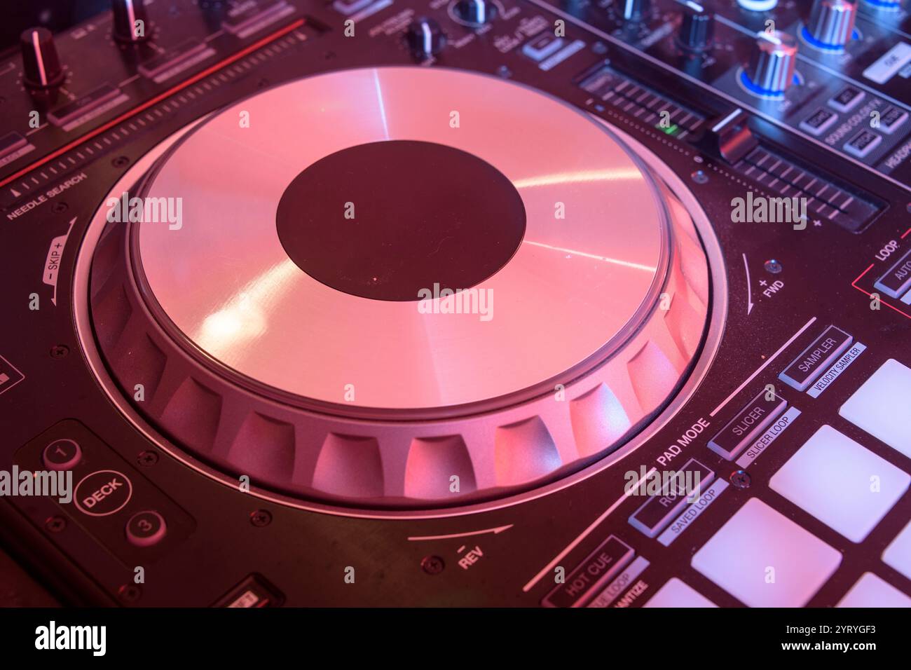Gros plan de la molette d'un contrôleur DJ illuminée par des lumières vibrantes, mettant l'accent sur la musique électronique, l'équipement DJ et l'atmosphère de la vie nocturne. Banque D'Images