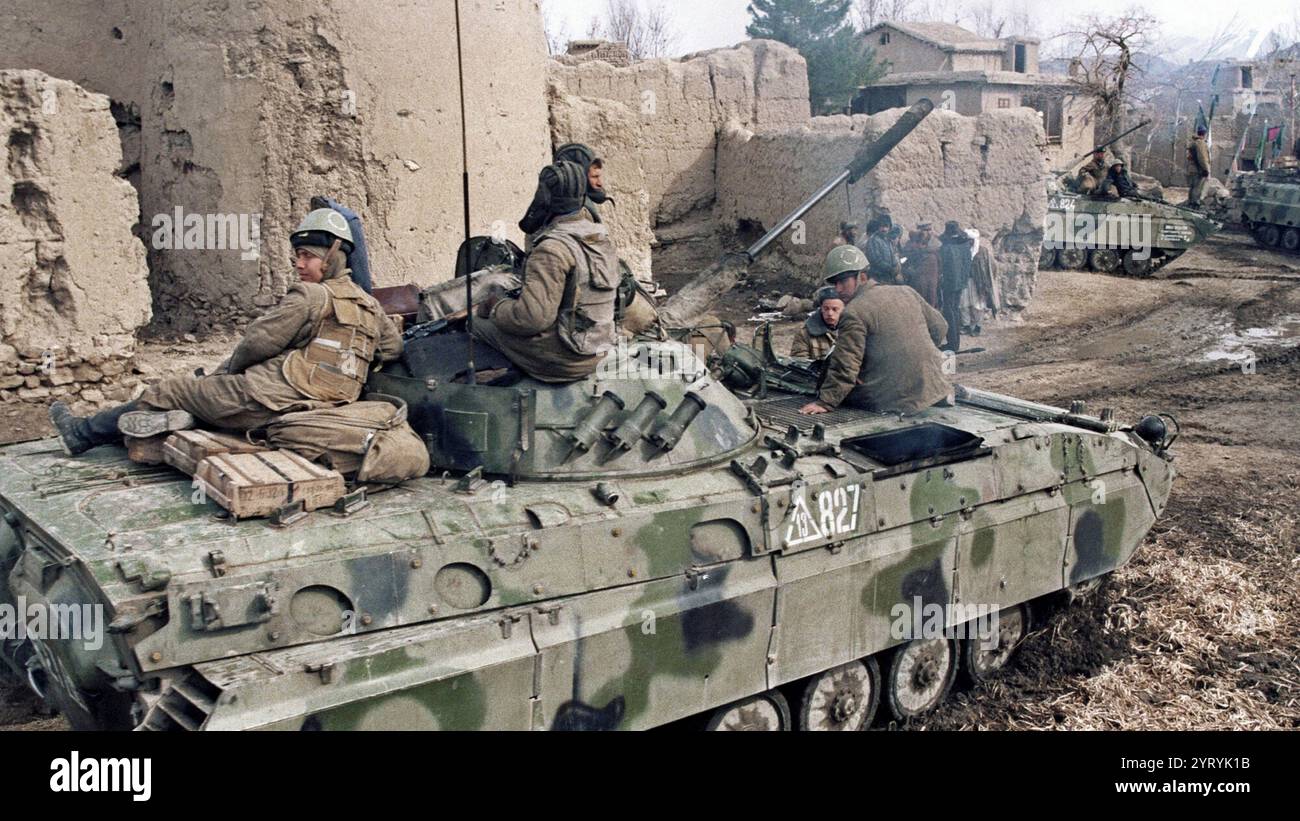 Des soldats soviétiques montent au sommet d'un char à travers un village afghan le 23 février 1988. Banque D'Images