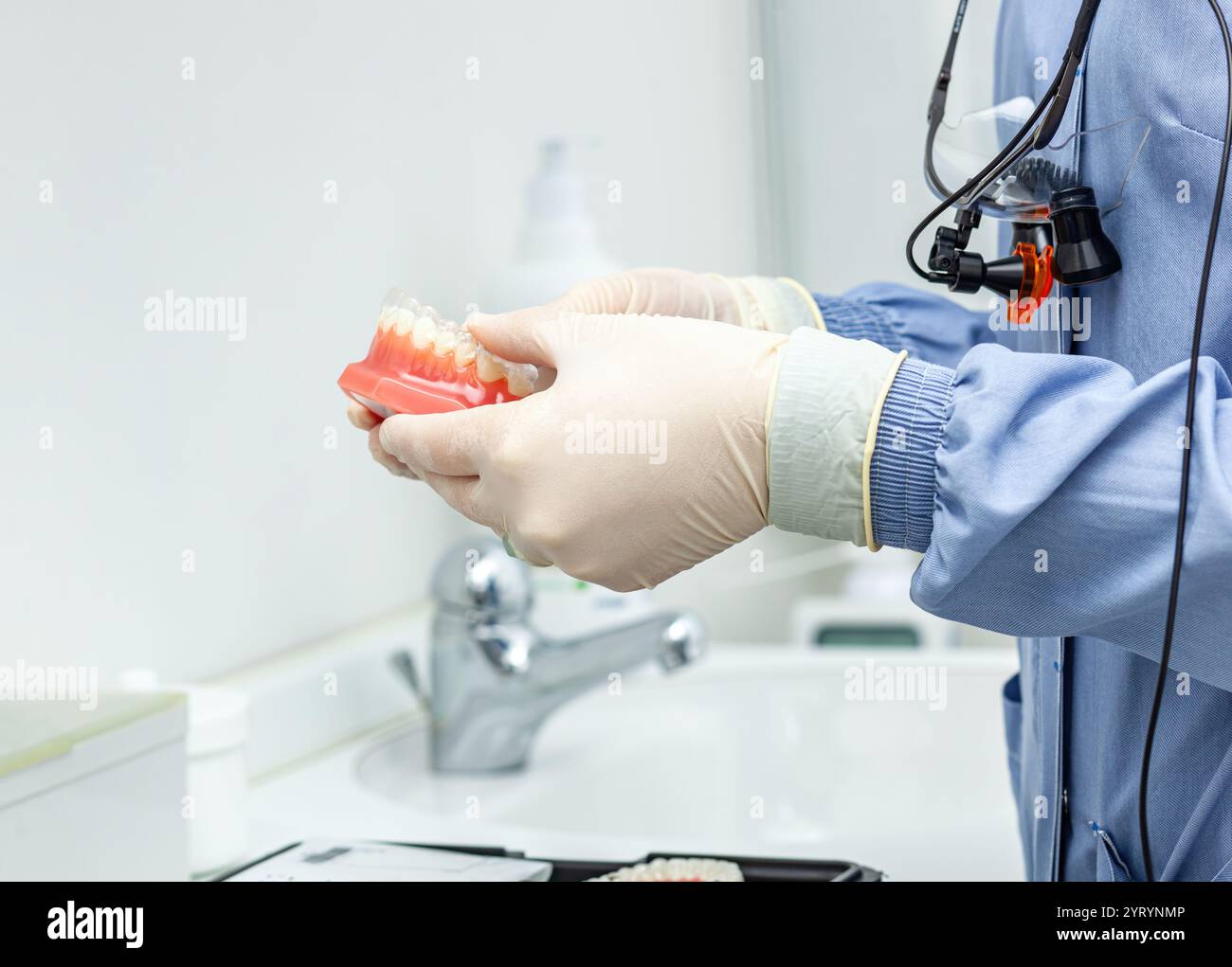 Dentiste portant des gants et une loupe examine un modèle de dents dans une clinique dentaire Banque D'Images