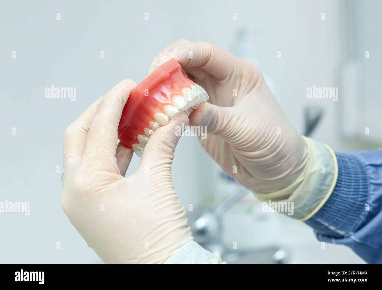 Dentiste portant des gants place soigneusement des appareils dentaires invisibles sur un modèle de dents détaillé dans un cadre de clinique dentaire moderne Banque D'Images