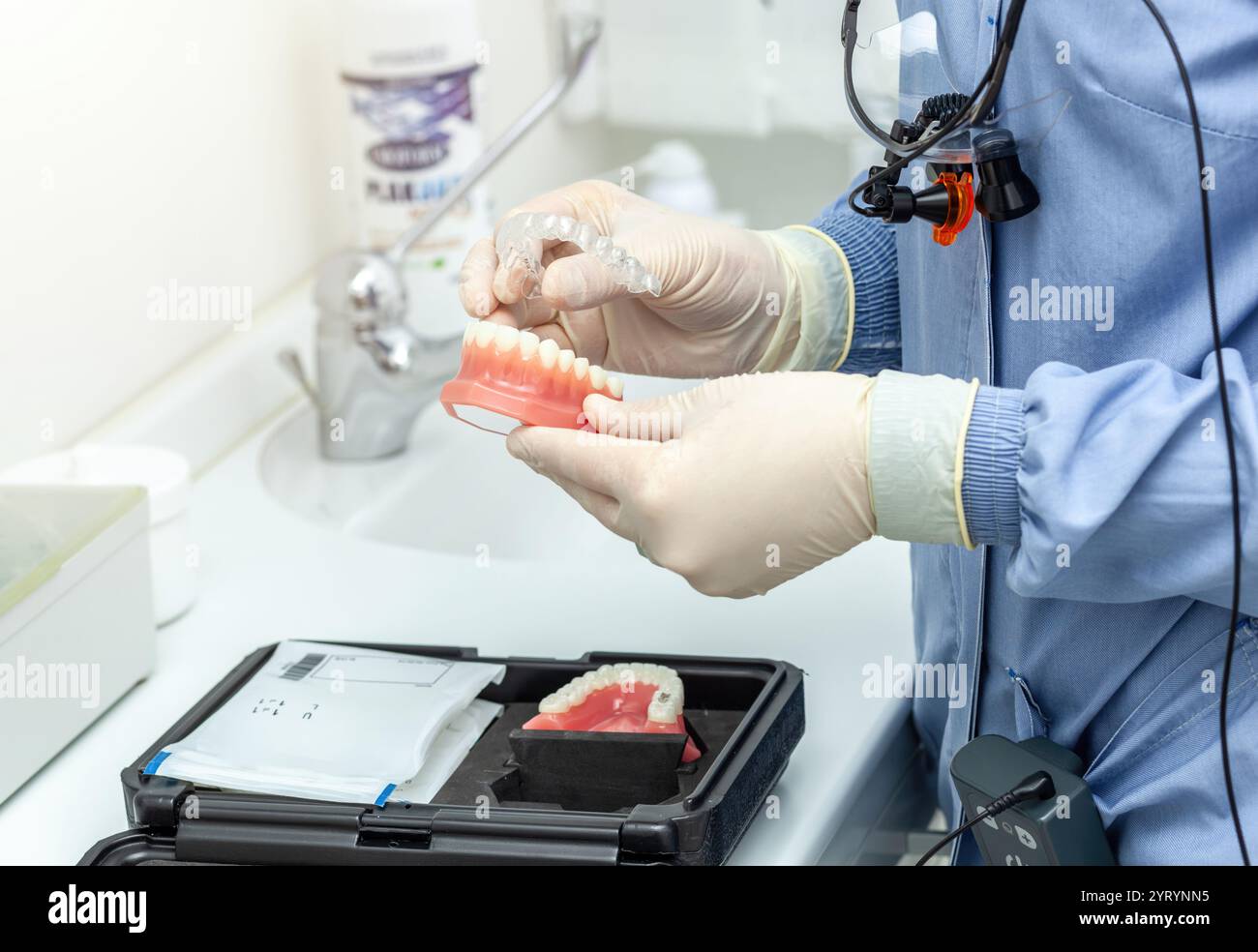 Dentiste portant une loupe et des gants plaçant des bagues invisibles alignent sur le moule dentaire dans une clinique dentaire Banque D'Images