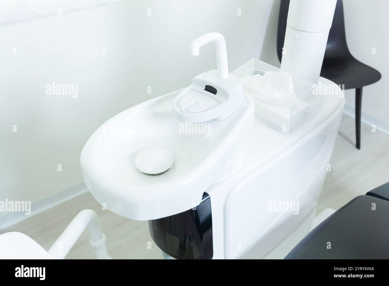 Lavabo blanc avec robinet et mouchoirs dans une clinique dentaire contemporaine, assurant le confort et l'hygiène du patient pendant les procédures dentaires Banque D'Images