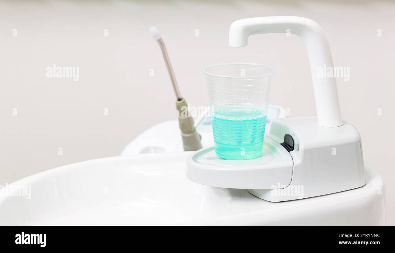 Gros plan d'un évier de crachage de chaise de dentiste avec une tasse de rince-bouche bleu et un jet d'eau, prêt pour le patient à rincer après une procédure dentaire Banque D'Images