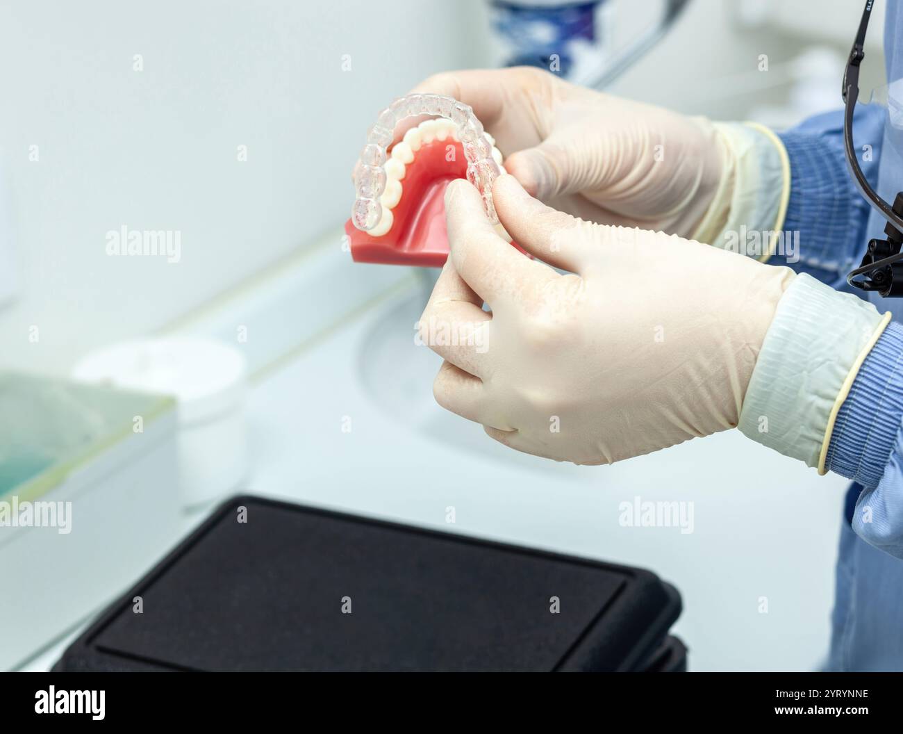 Dentiste portant des gants tenant un modèle de dents avec des bagues invisibles démontrant l'alignement des dents dans une clinique dentaire Banque D'Images