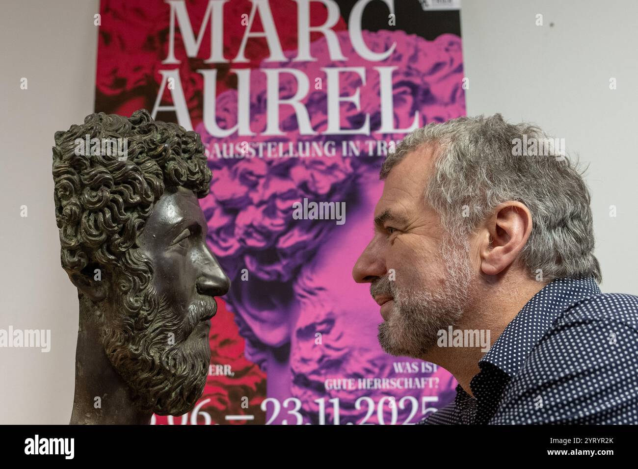 Trèves, Allemagne. 04th Dec, 2024. Marcus Reuter, directeur du Rheinisches Landesmuseum de Trèves, regarde dans la caméra devant une affiche pour l'exposition d'État à côté d'une réplique de la tête de l'empereur romain Marc Aurèle. L’exposition au Rheinisches Landesmuseum et au Stadtmuseum Trèves se déroule du 15 juin au 23 novembre 2025. Crédit : Harald Tittel/dpa/Alamy Live News Banque D'Images