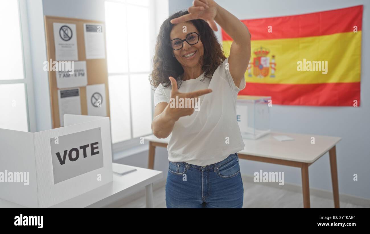 Femme gestuelle cadre photo avec les mains dans un collège électoral intérieur en espagne avec une cabine de vote et drapeau espagnol en arrière-plan Banque D'Images