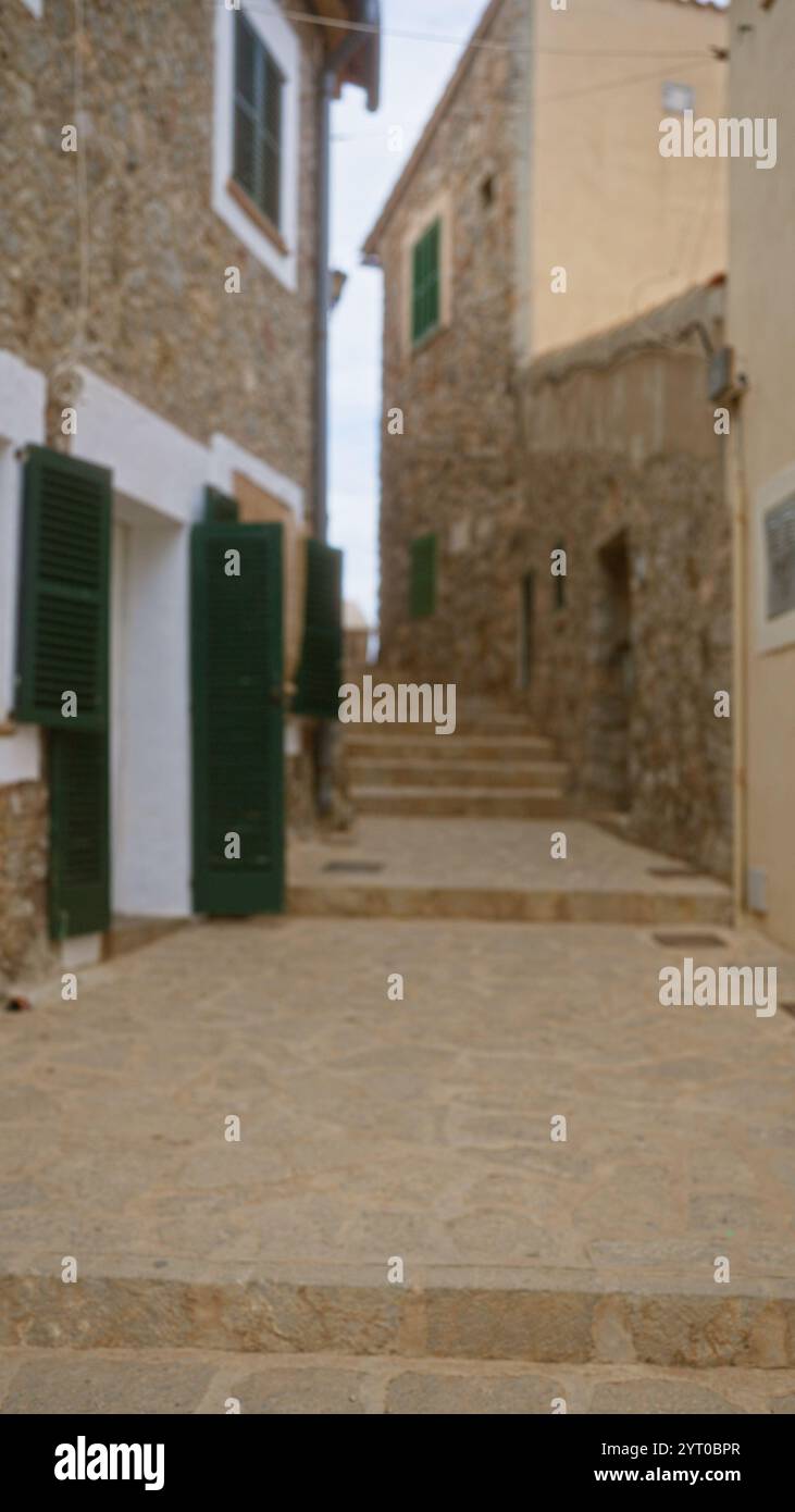 Scène extérieure floue à majorque, en espagne, avec une vue défocalisée sur des bâtiments en pierre rustiques avec des volets verts et des marches en pierre dans une allée étroite Banque D'Images