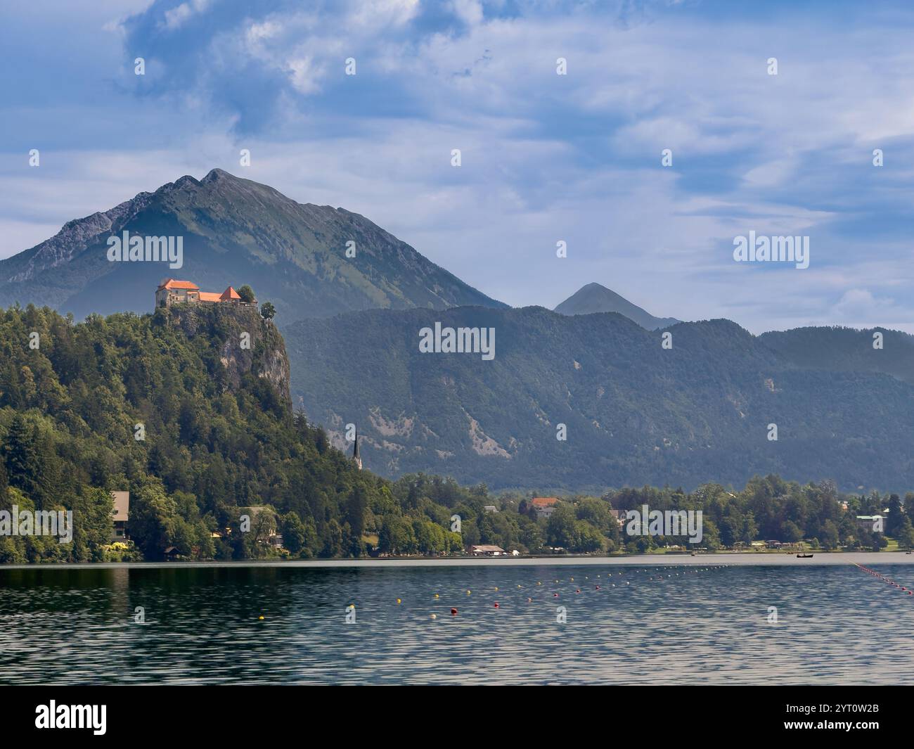 Lac de Bled, Slovénie - 28 juin 2024 : le château médiéval de Bled avec ses toits rouges se dresse au-dessus du lac sur sa roche boisée sous un paysage nuageux bleu. Foreste Banque D'Images