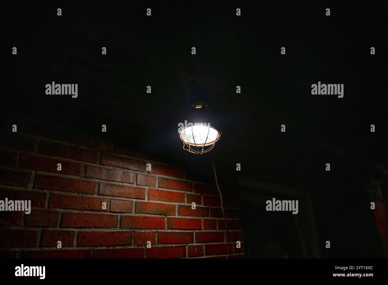 Un luminaire chaud est suspendu au plafond, projetant une lueur douce sur un mur de briques rustique. L'atmosphère est morose et évocatrice, mettant en valeur un Industri Banque D'Images