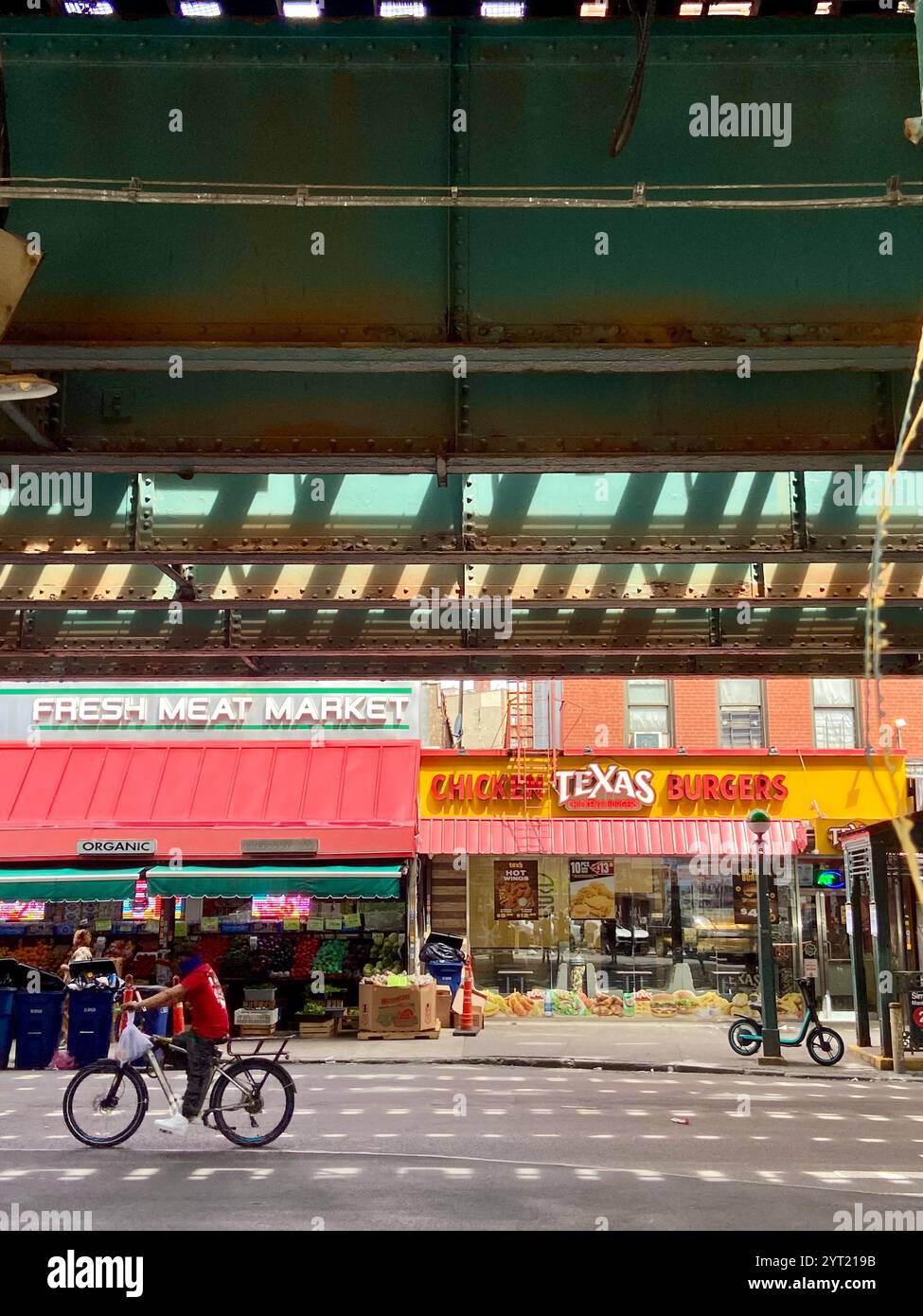 New York, États-Unis - 2 juin 1024 : cycliste dans Bronx Street scène avec des voies ferrées surélevées et des vitrines locales Banque D'Images