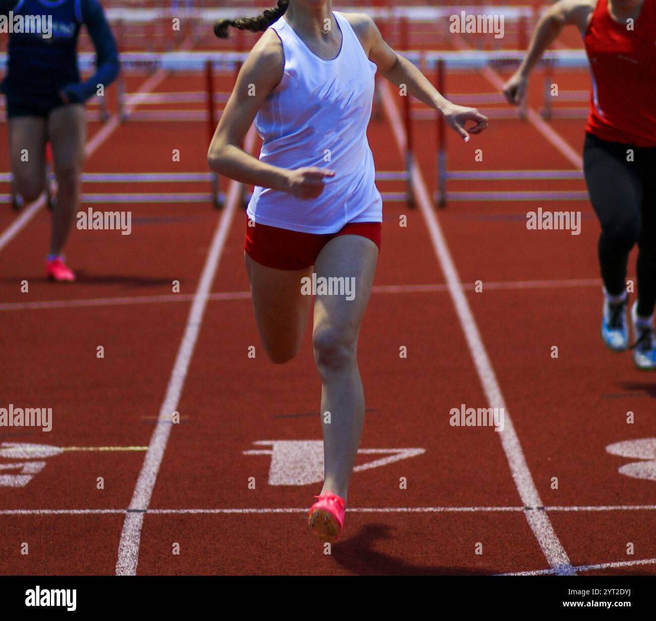 Une jeune femme court vers la ligne d'arrivée dans une course de haies, montrant sa détermination et sa vitesse. Banque D'Images