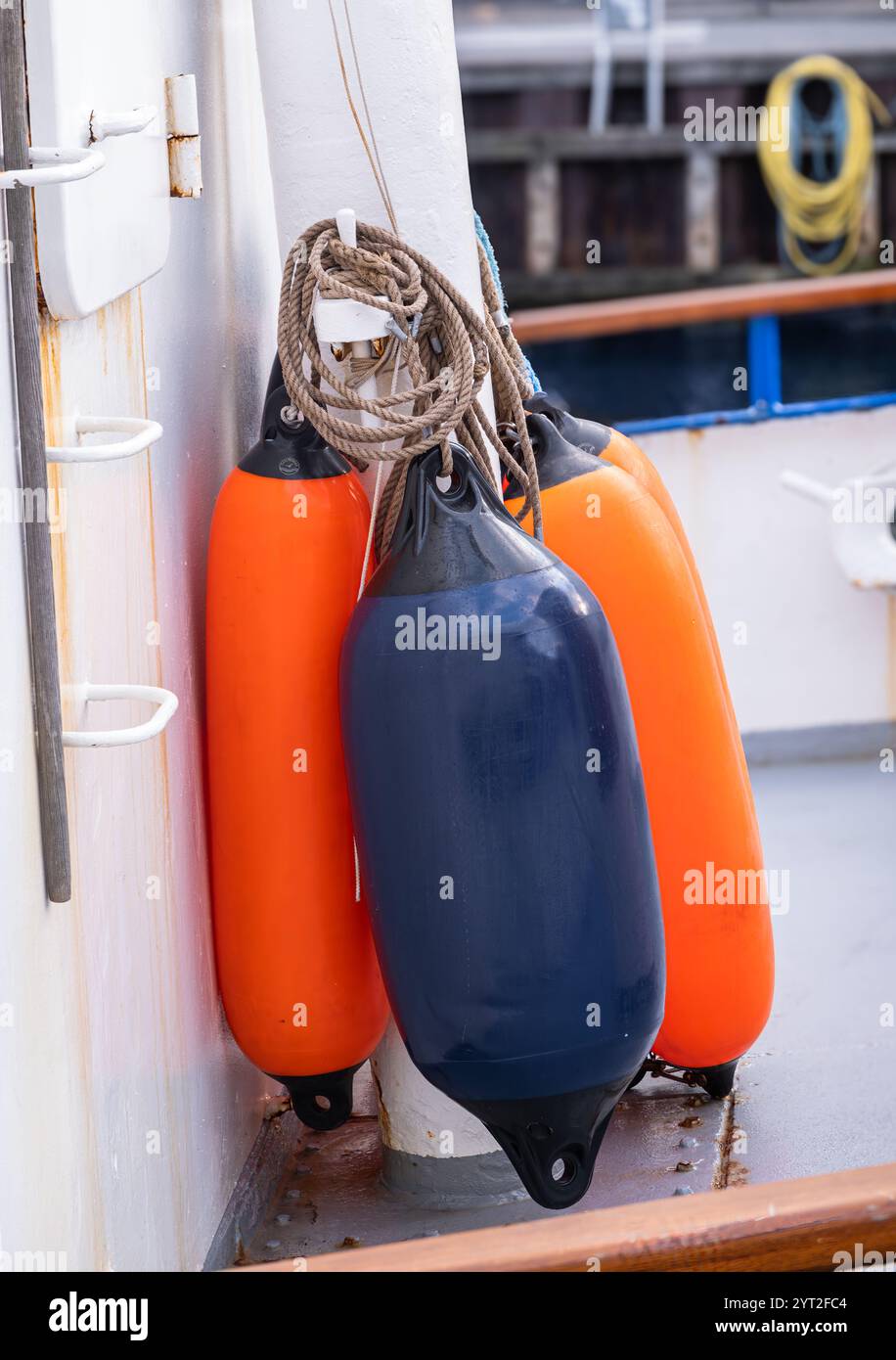 Gros plan des défenses d'un bateau, présentant des bouées orange et bleues durables fixées à un poteau. Banque D'Images