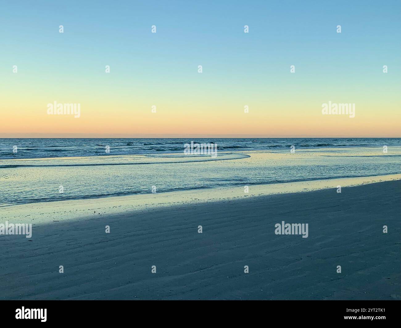 Des vagues douces roulent le long d'un rivage vide sous un ciel pastel, capturant la beauté tranquille de tôt le matin sur une plage paisible. - Image de stock capturée avec un smartphone