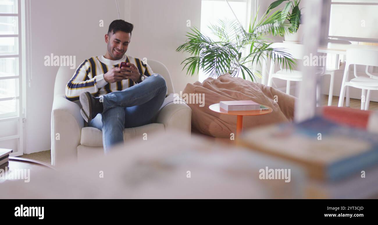 Vue de face d'un homme biracial heureux travaillant dans un bureau créatif, parlant sur le smartphone et smili Banque D'Images