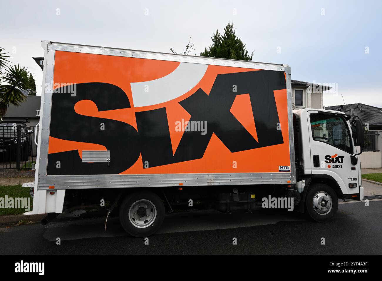 Côté d'un camion de location Sixt, un Isuzu NPR 45 155, garé dans une rue de banlieue tard par un jour de pluie, avec sa marque orange vif qui se démarque Banque D'Images