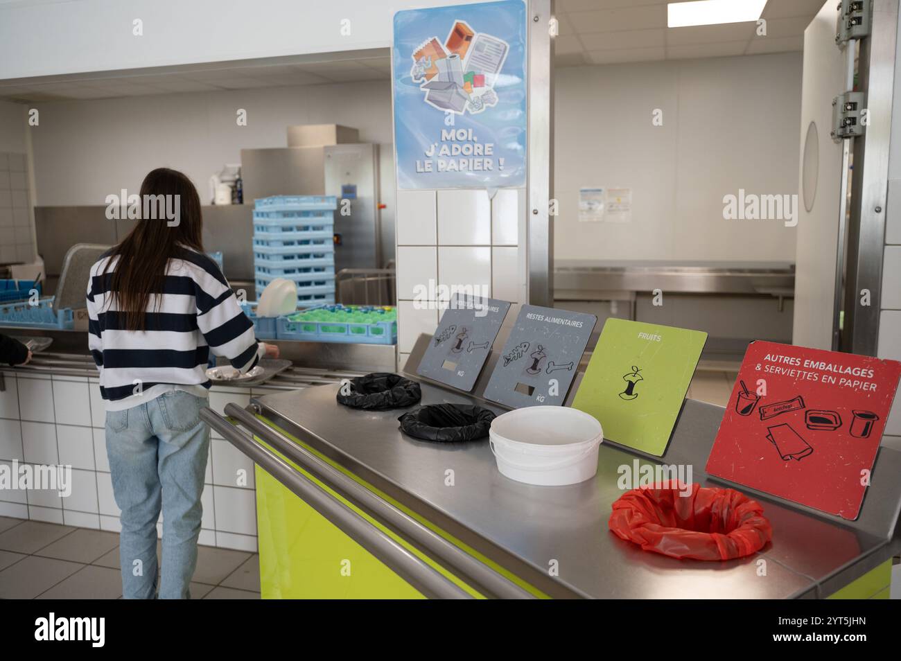 Restauration institutionnelle : une écolière près des poubelles de tri dans une cafétéria scolaire, triant les déchets après avoir terminé le déjeuner. Tri des aliments et non-fo Banque D'Images