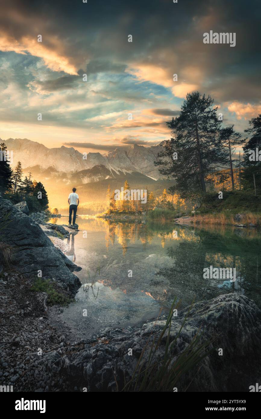 Randonneur profitant du paysage matinal incroyable sur un lac magnifique dans les Alpes bavaroises, avec les montagnes et les nuages spectaculaires du lever du soleil reflétés dans th Banque D'Images