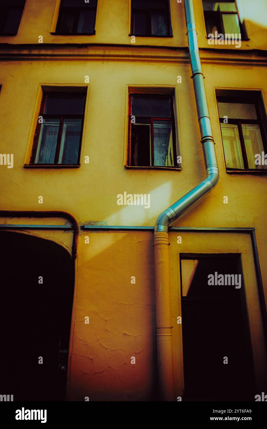 Photo d'un ancien bâtiment en pierre avec des fenêtres sombres et un tuyau d'évacuation, situé dans la partie historique de la cour de la ville. Banque D'Images
