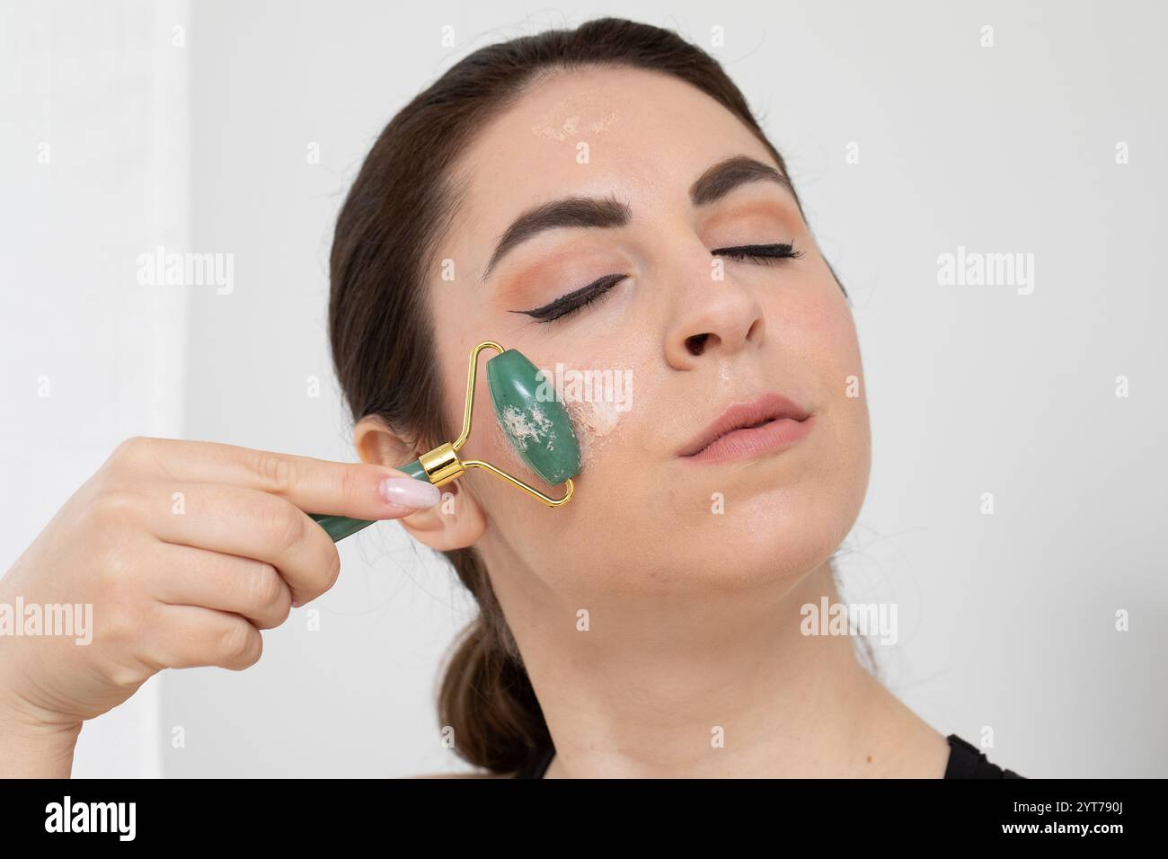 Esthéticienne massant la peau du visage avec rouleau de jade pour le soulèvement anti-âge et la tonification Banque D'Images