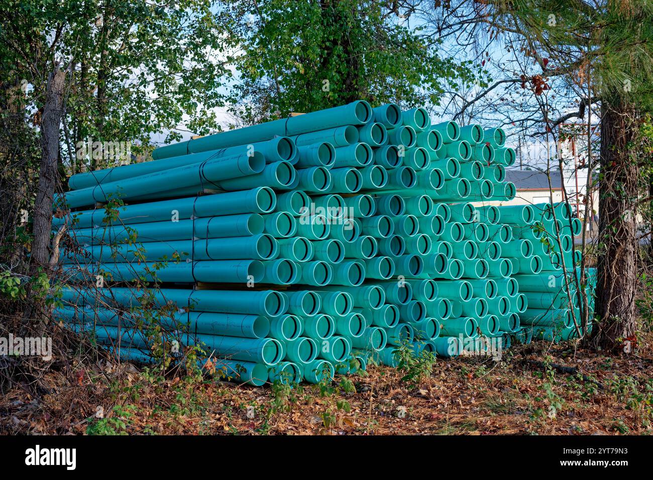 Regroupements de tuyaux d'égout en pvc neufs empilés haut avec des cerclages assis sous quelques arbres à l'ombre en attente d'être installés pour un nouveau develo Banque D'Images Regroupements de tuyaux d'égout en pvc neufs empilés haut avec des cerclages assis sous quelques arbres à l'ombre en attente d'être installés pour un nouveau develo Banque D'Images
