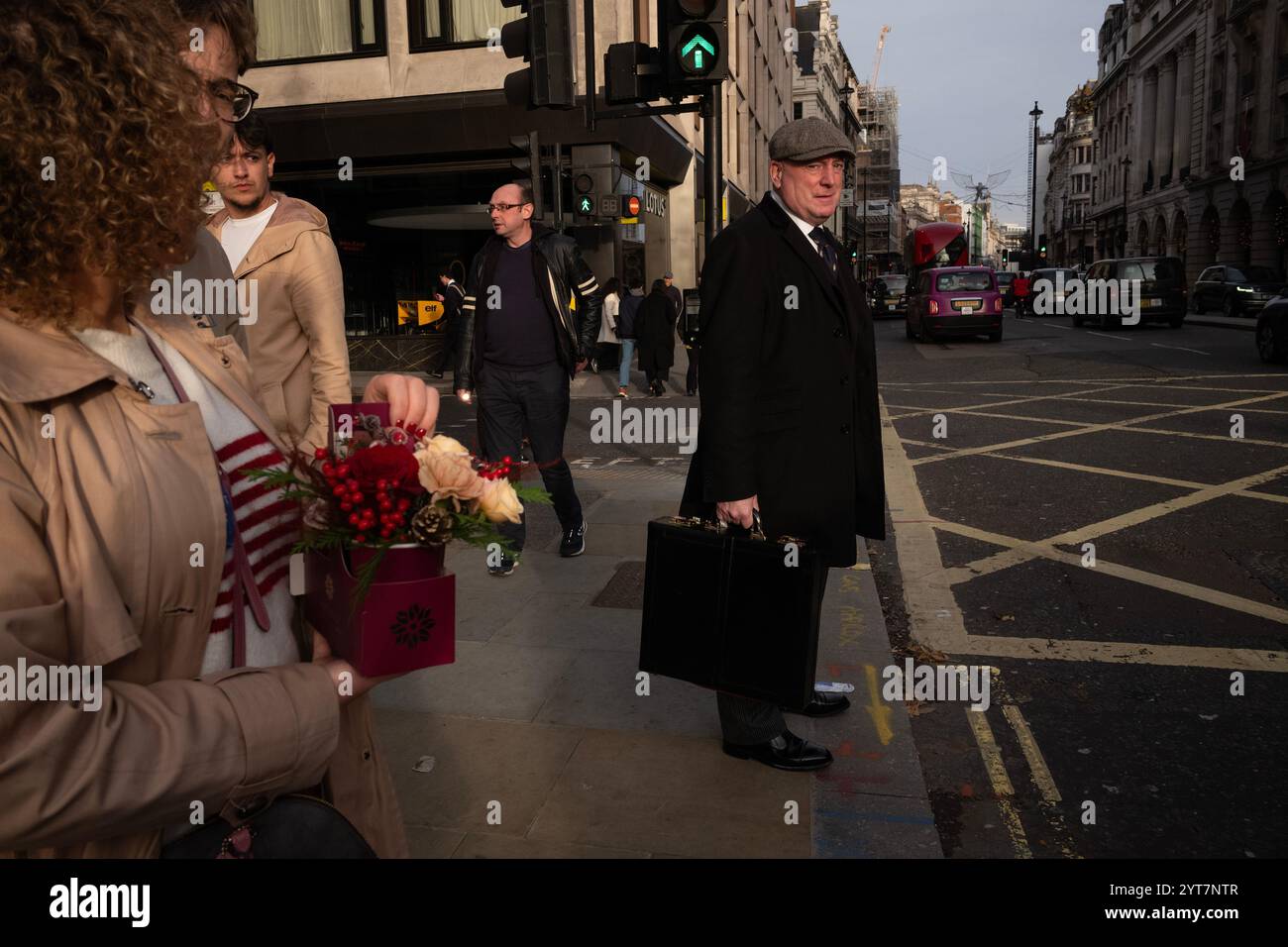Ouvrier municipal portant une casquette plate, tenant une grande mallette attendant à un passage piétonnier le long de Piccadilly, au cœur de Mayfair, novembre 2024 Banque D'Images