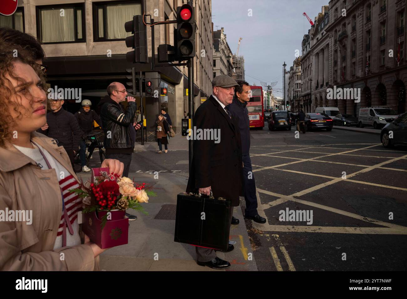 Ouvrier municipal portant une casquette plate, tenant une grande mallette attendant à un passage piétonnier le long de Piccadilly, au cœur de Mayfair, novembre 2024 Banque D'Images