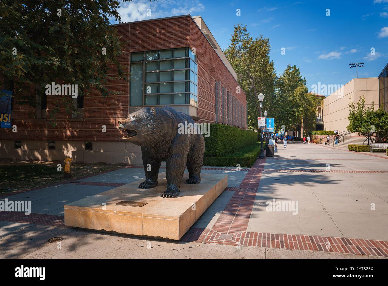 La statue de l'ours Bruin se dresse sur un piédestal de pierre à UCLA, entourée de verdure et d'un bâtiment moderne en briques, sous un ciel bleu clair. Banque D'Images