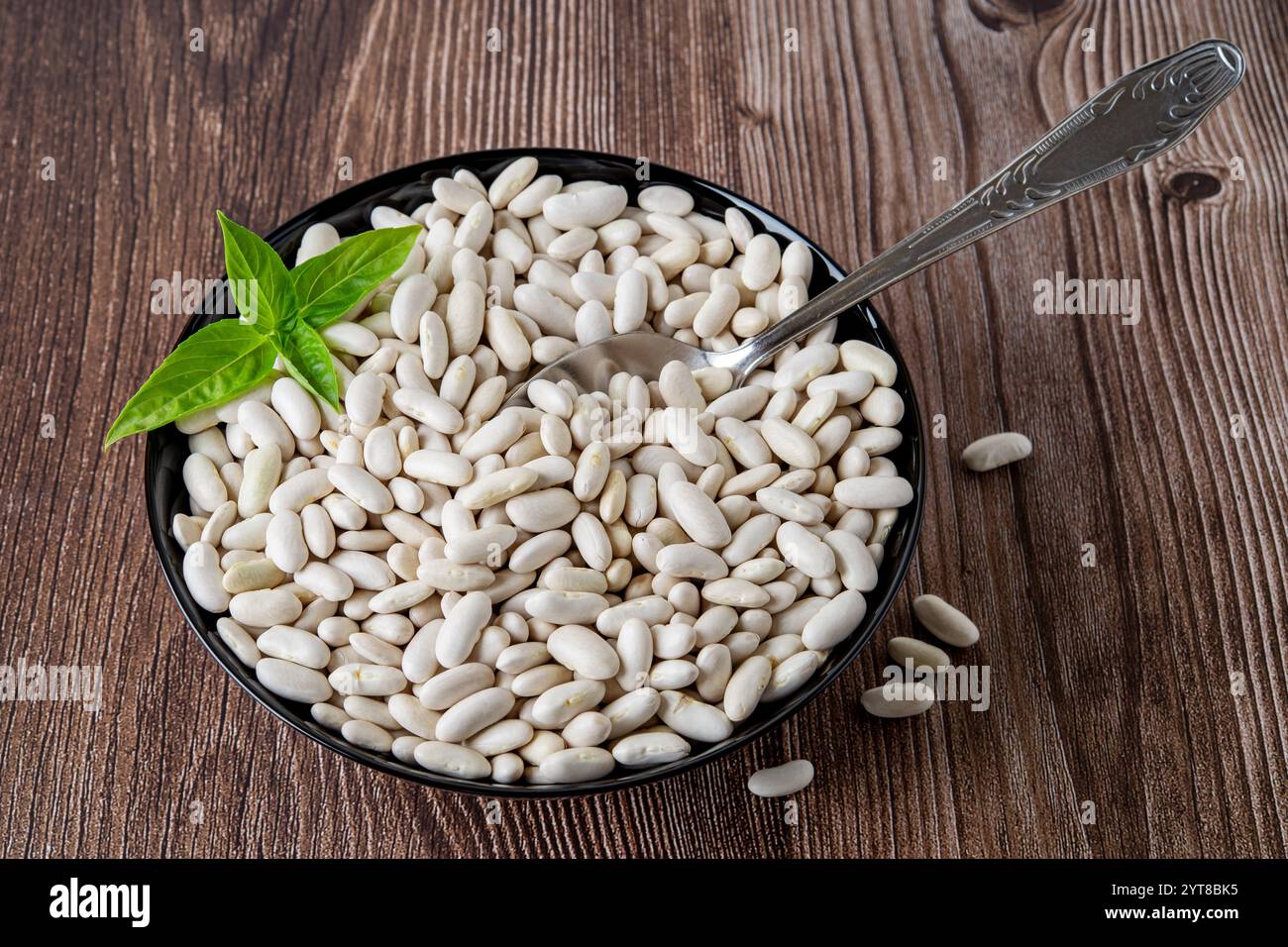 Haricots blancs dans un bol noir sur fond de bois brun. Haricots rouges biologiques crus ou haricot préparés pour la cuisson des haricots verts végétariens. Récolte. Banque D'Images