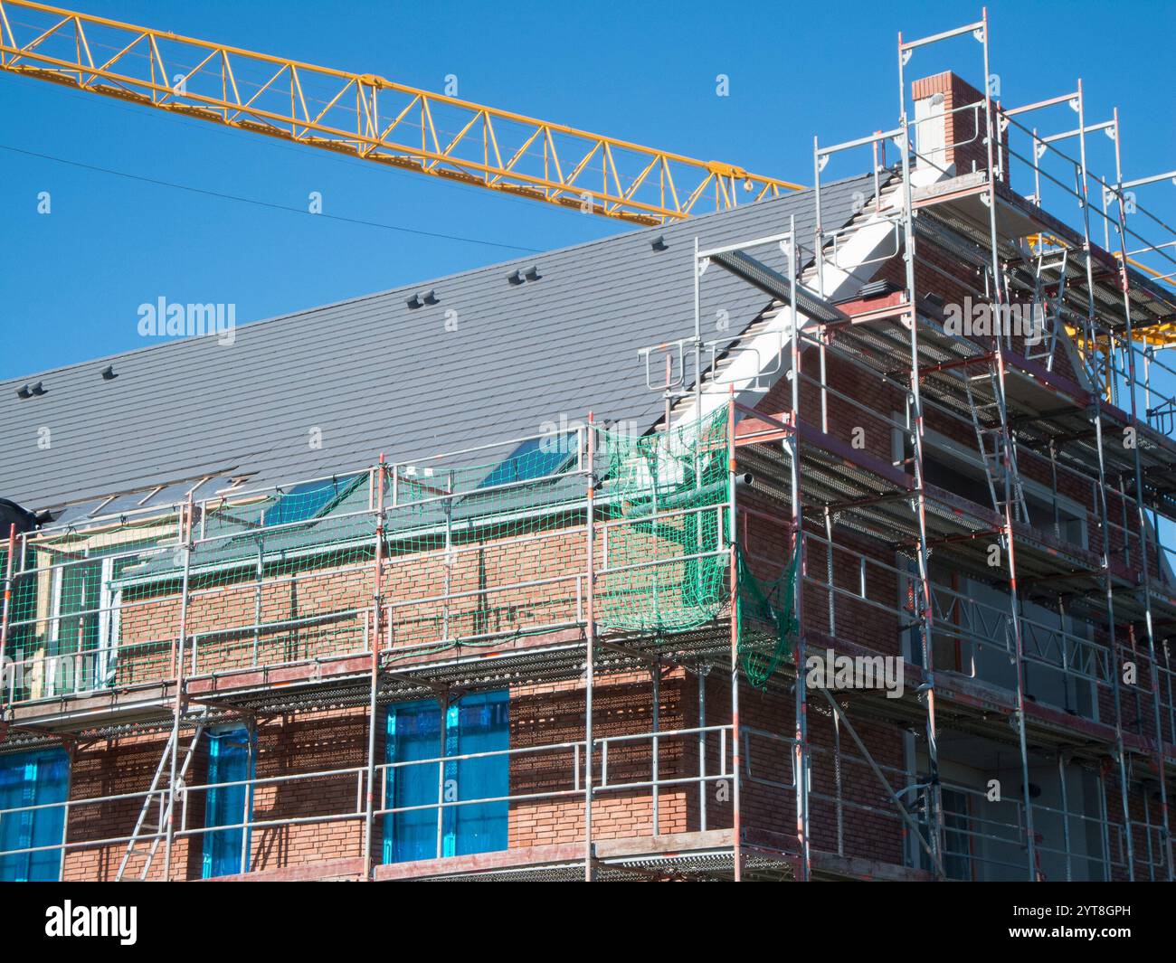 Vue partielle de l'échafaudage sur un bâtiment de plusieurs étages nouvellement construit avec parement de briques et flèche de grue jaune contre un ciel bleu. Banque D'Images