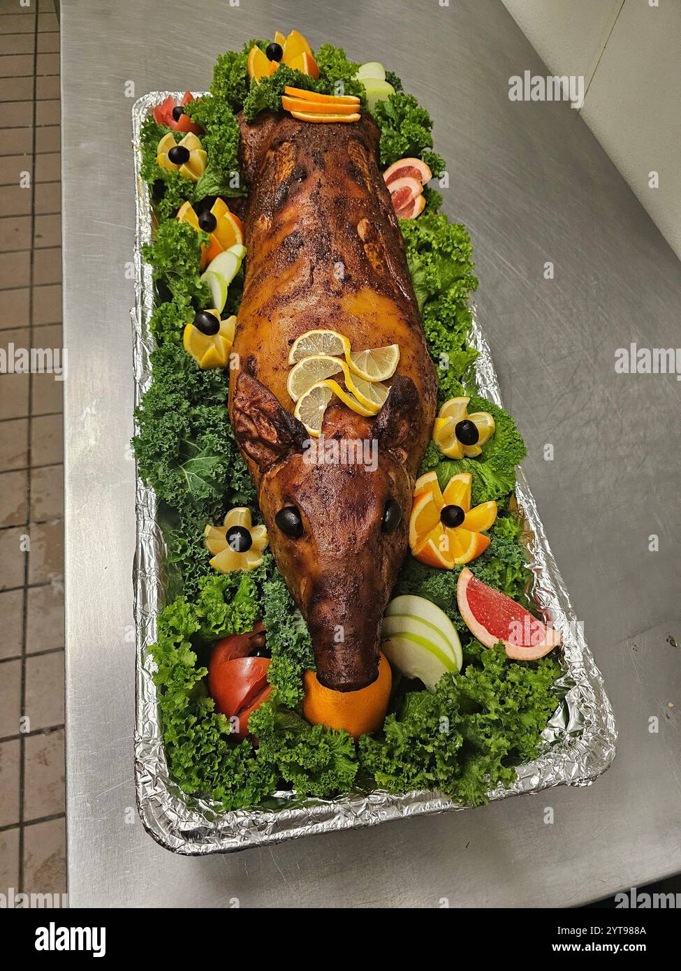 Porc entier rôti servi sur un plateau décoratif entouré de fruits frais et de laitue, présenté comme une pièce maîtresse de fête pour une célébration. Banque D'Images