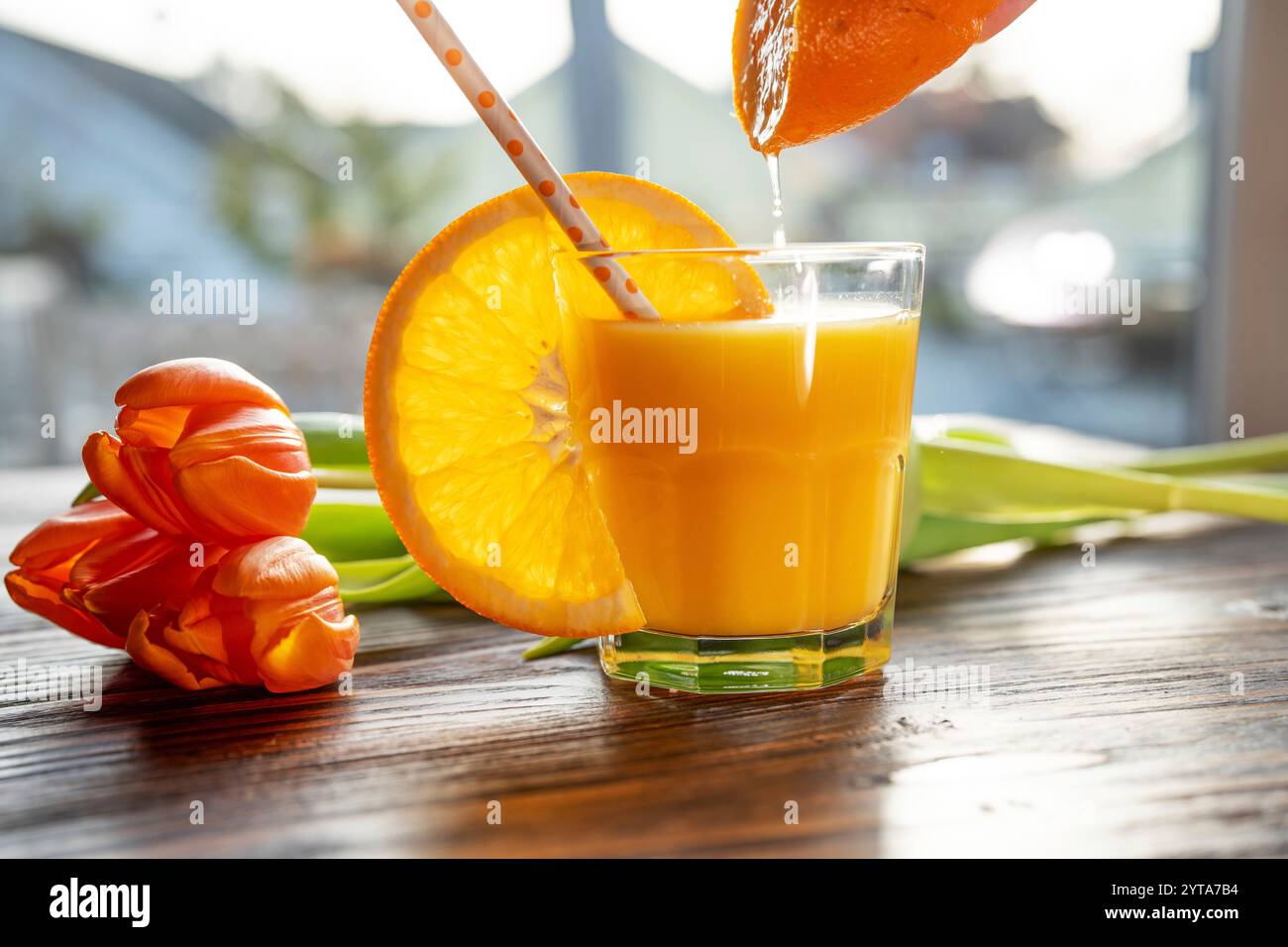 Verre de jus d'orange fraîchement pressé avec une tranche d'orange et un bouquet de tulipes sur une table en bois. Gros plan avec une faible profondeur de champ. Banque D'Images
