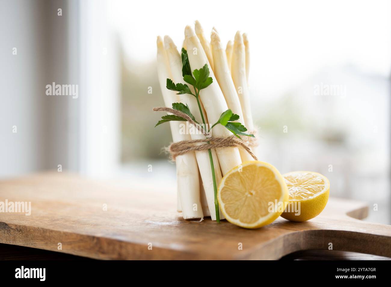 Bouquet debout d'asperges blanches fraîches. Légumes de printemps de saison avec persil et citron sur planche à découper en bois. Scène de cuisine pour la gastronomie saisonnière. Banque D'Images