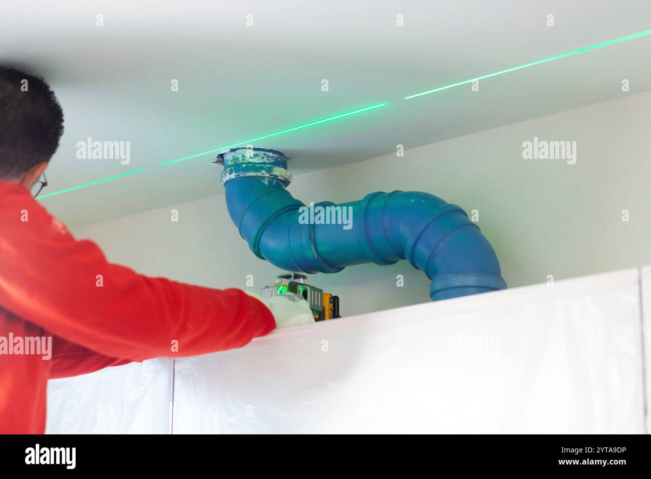 Un plâtreur prend des mesures avec un niveau laser pour créer un mur au-dessus des armoires de cuisine Banque D'Images