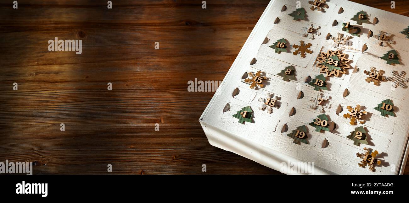 Calendrier de l'Avent fait maison sur bois sombre. Emballage blanc pour 24 petites surprises cadeaux fabriquées à partir de matériaux renouvelables. Fond horizontal de noël pour les salutations et la bannière de l'Avent. Vue de dessus avec espace pour le texte. Banque D'Images