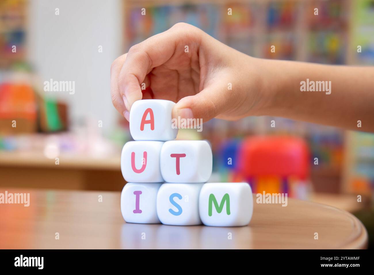 Une main d'enfant plaçant un cube blanc avec la lettre 'A' au-dessus d'une pyramide de cubes orthographiant 'AUTISME', soulignant la conscience et la compréhension de au Banque D'Images