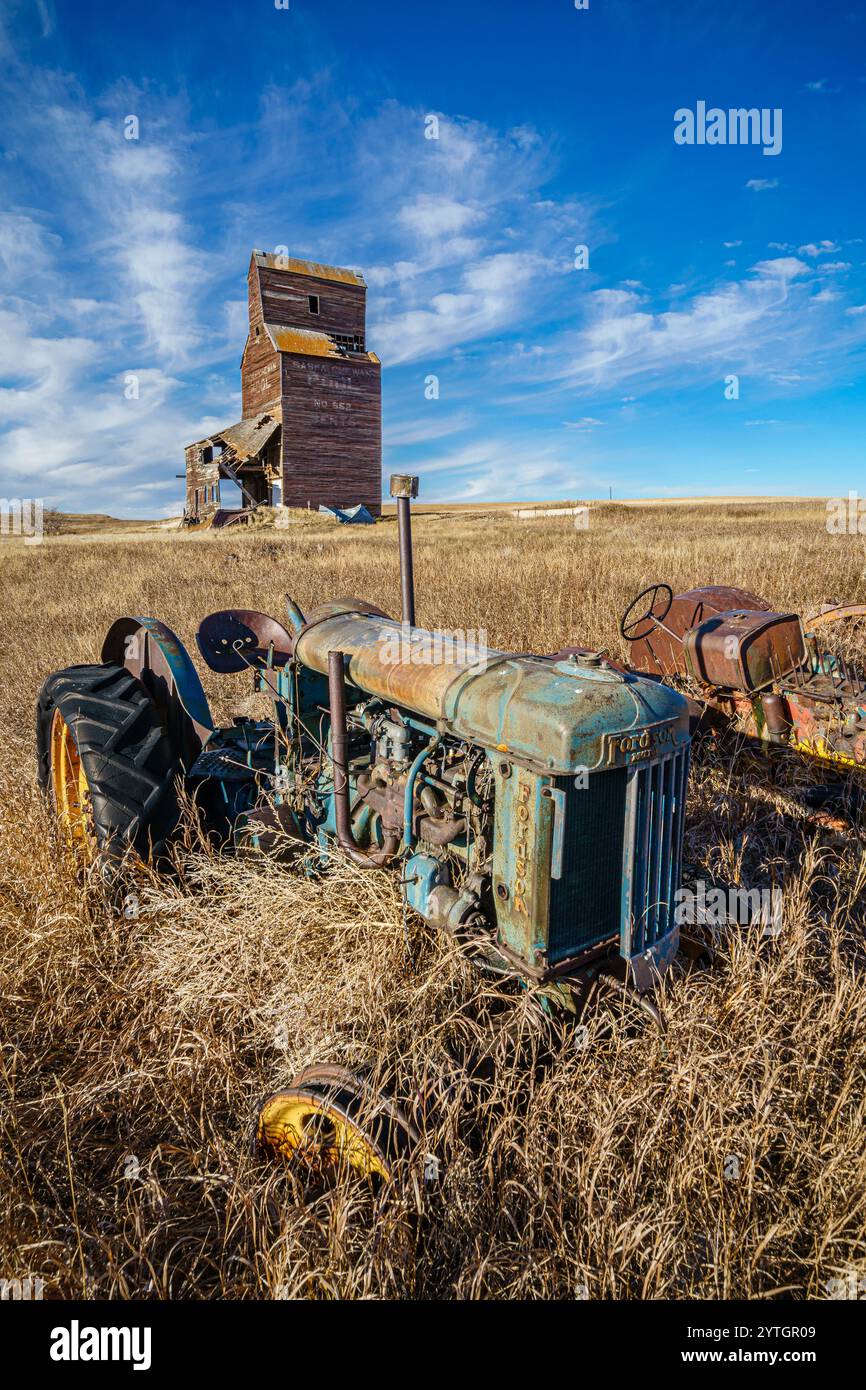 Un vieux tracteur bleu est assis dans un champ d'herbes hautes. Le tracteur est entouré de nombreuses mauvaises herbes et le champ est sec et aride. La scène donne Banque D'Images