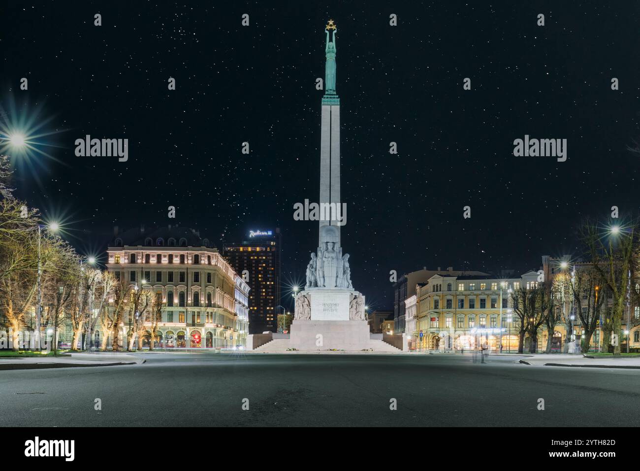 Le monument de la liberté à Riga la nuit, debout sous un ciel étoilé, entouré de bâtiments historiques et de lampadaires éclairés. Lettonie Banque D'Images