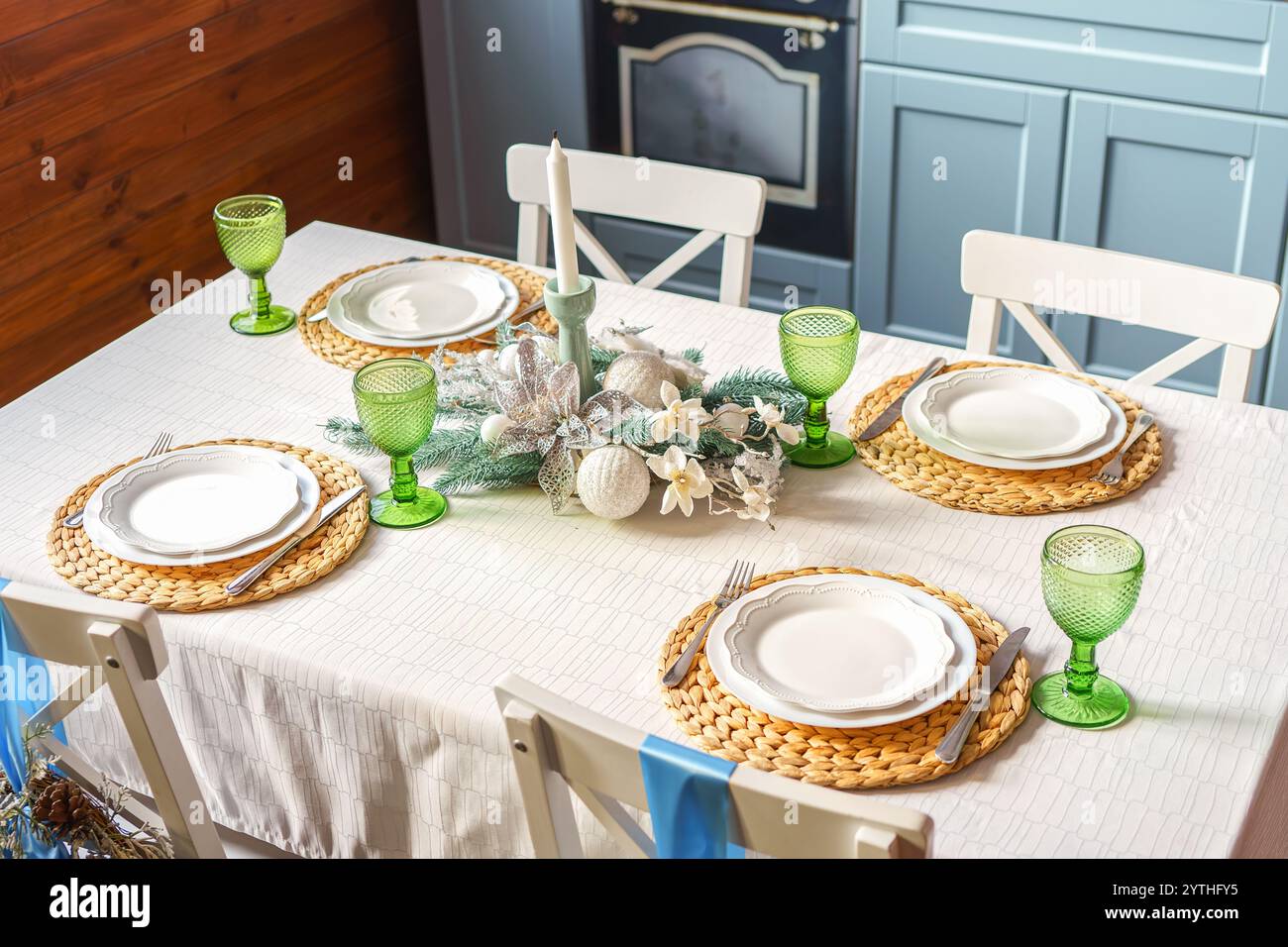 La table à manger des fêtes est élégamment agencée avec des verres verts, des sets de table tissés et des assiettes blanches, créant un cadre chaleureux et accueillant sur le kitche moderne Banque D'Images