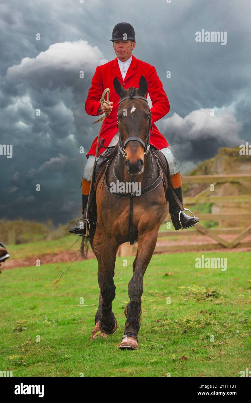 chasseur en manteau rouge montant son cheval vers la caméra avec un ciel orageux Banque D'Images