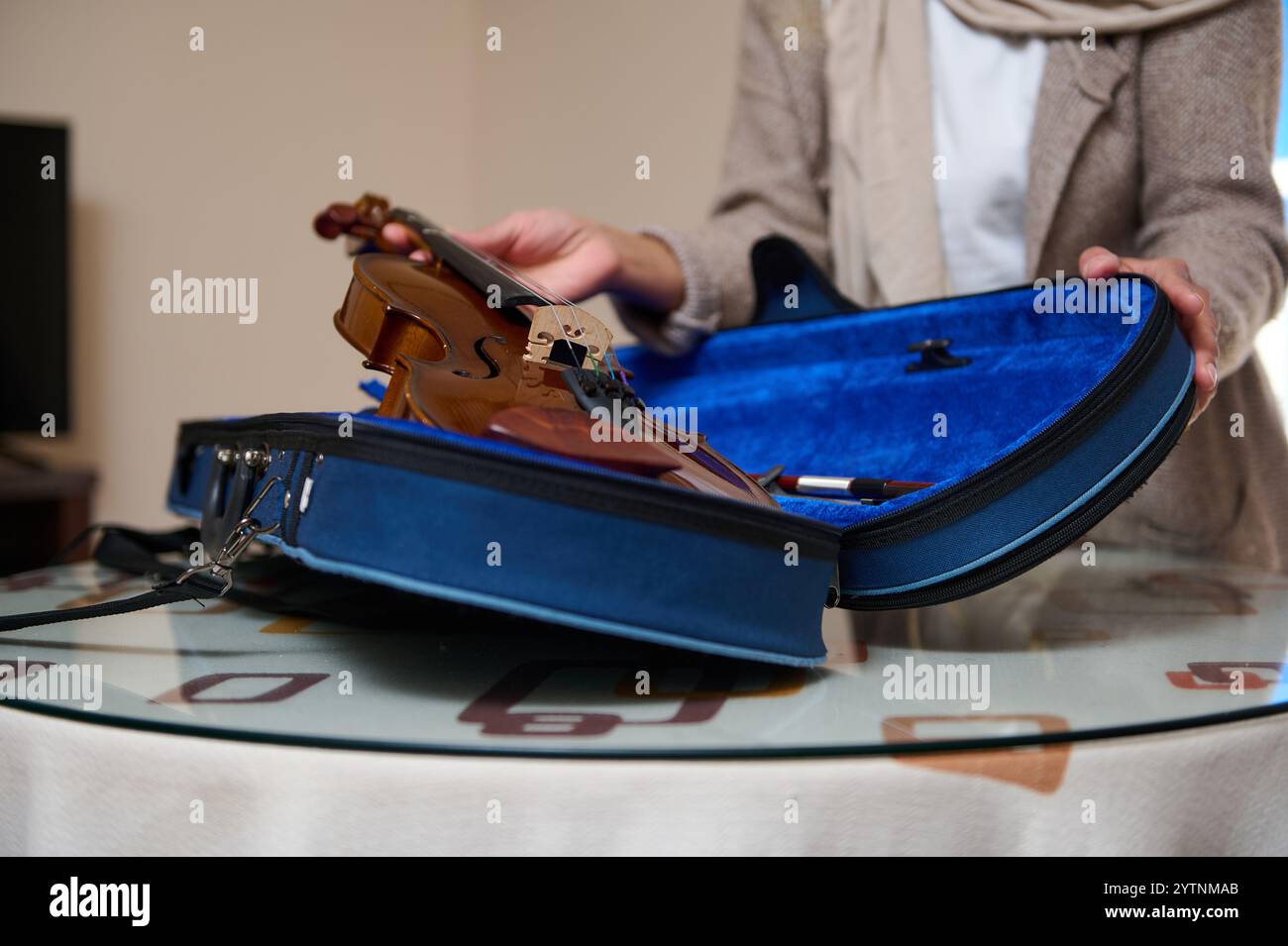 Une personne manipule doucement un violon, le plaçant dans un étui bleu souple sur une table. La scène suggère le soin, la protection, et l'importance de l'inst musical Banque D'Images