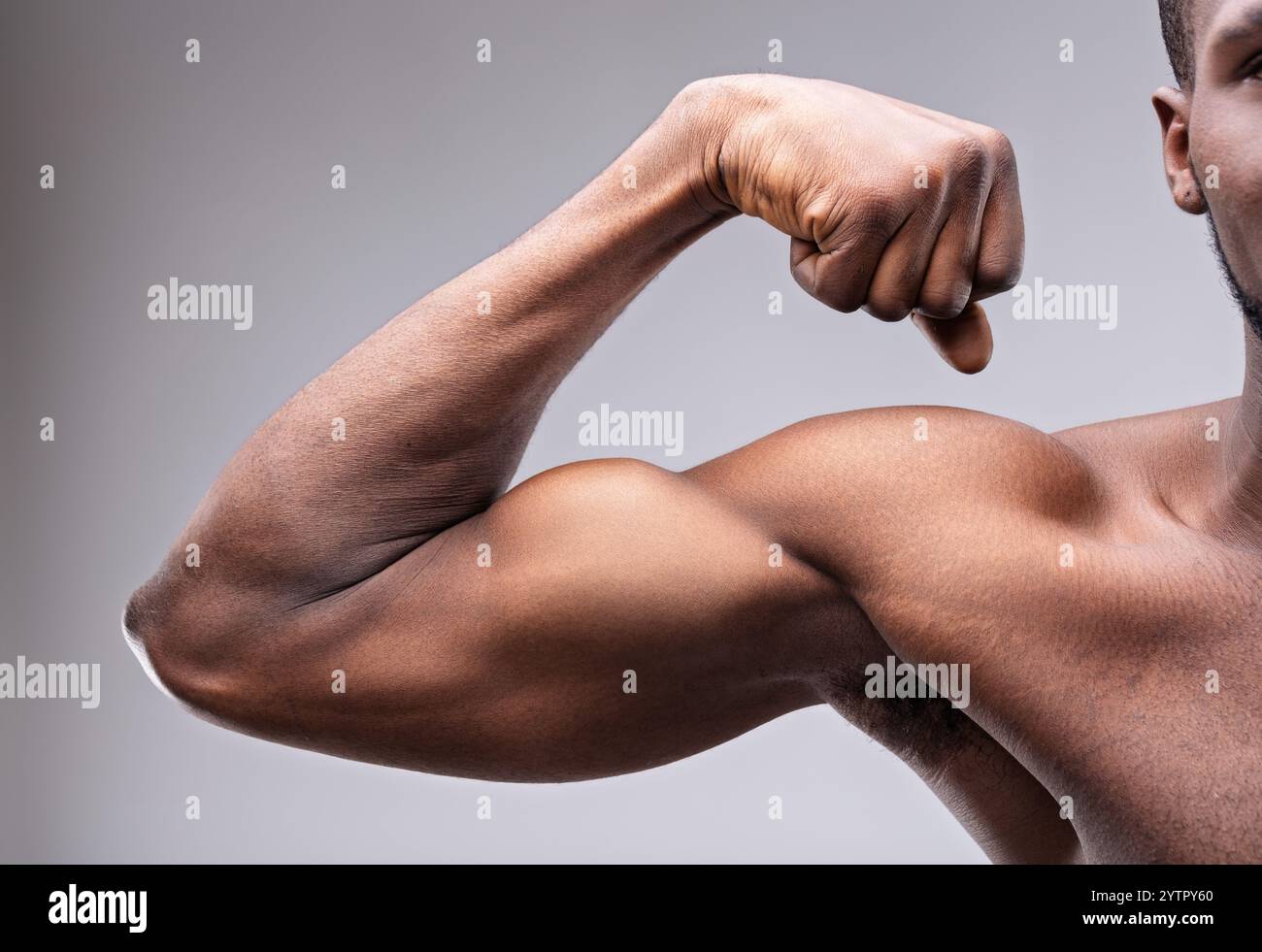 Gros plan d'un homme noir musclé qui fléchit ses biceps impressionnants, mettant en évidence la force et la forme physique sur un fond gris lisse, incarnant la puissance et Banque D'Images