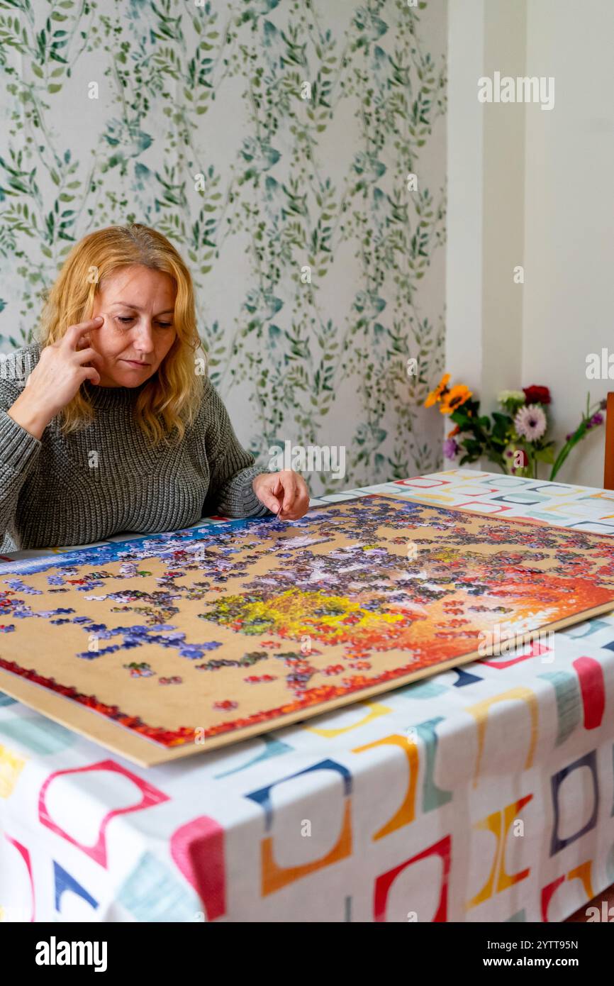 Image verticale d'une jolie femme caucasienne dans ses 40 ans faisant un puzzle dans le salon de sa maison. Concept de divertissement Banque D'Images