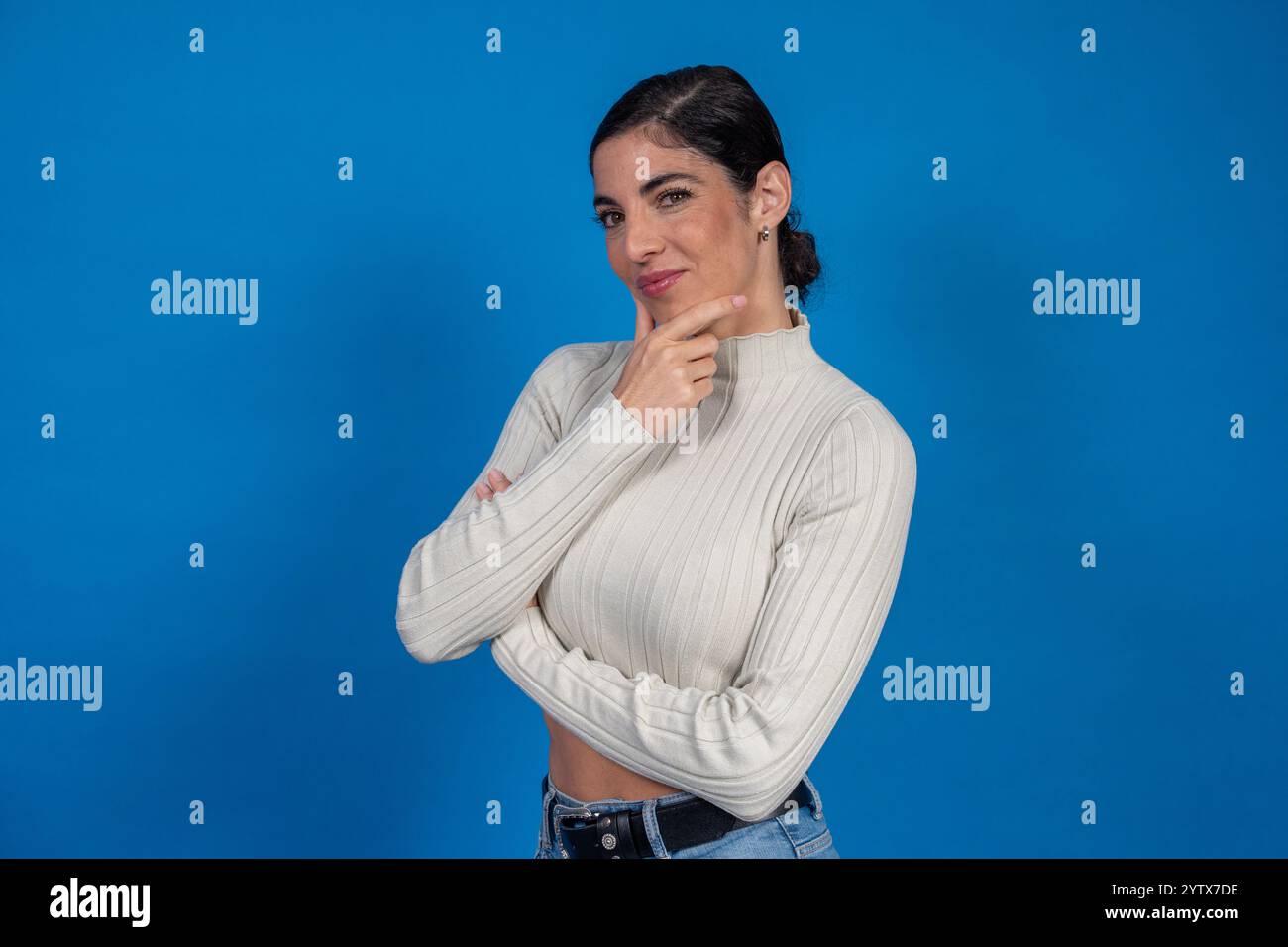 Portrait studio d'une jeune femme réfléchie avec les bras croisés touchant son menton sur un fond bleu vif Banque D'Images