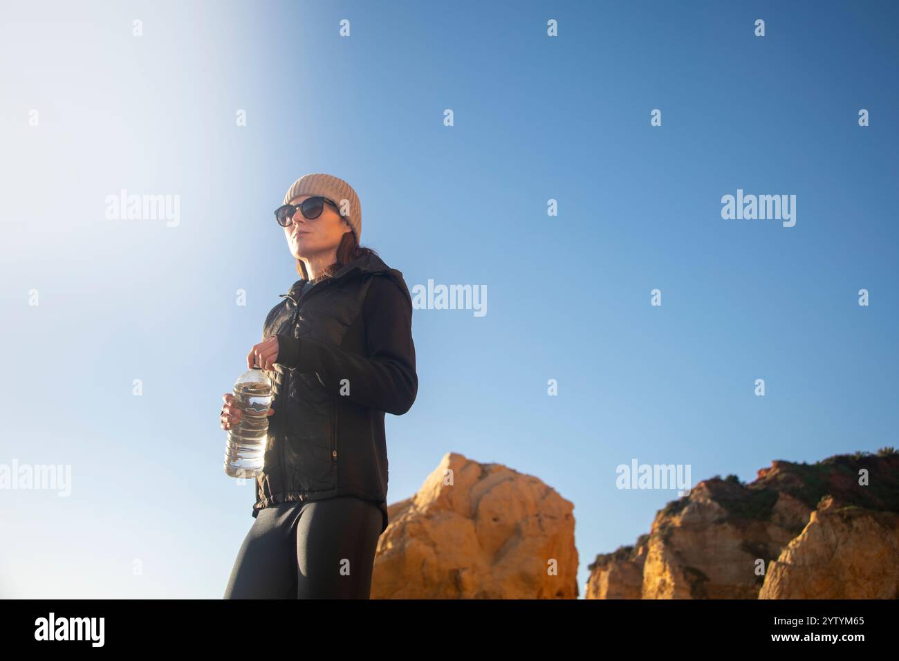 Coureuse sportive tenant une bouteille d'eau, s'entraînant à l'extérieur sous le soleil d'hiver. Banque D'Images