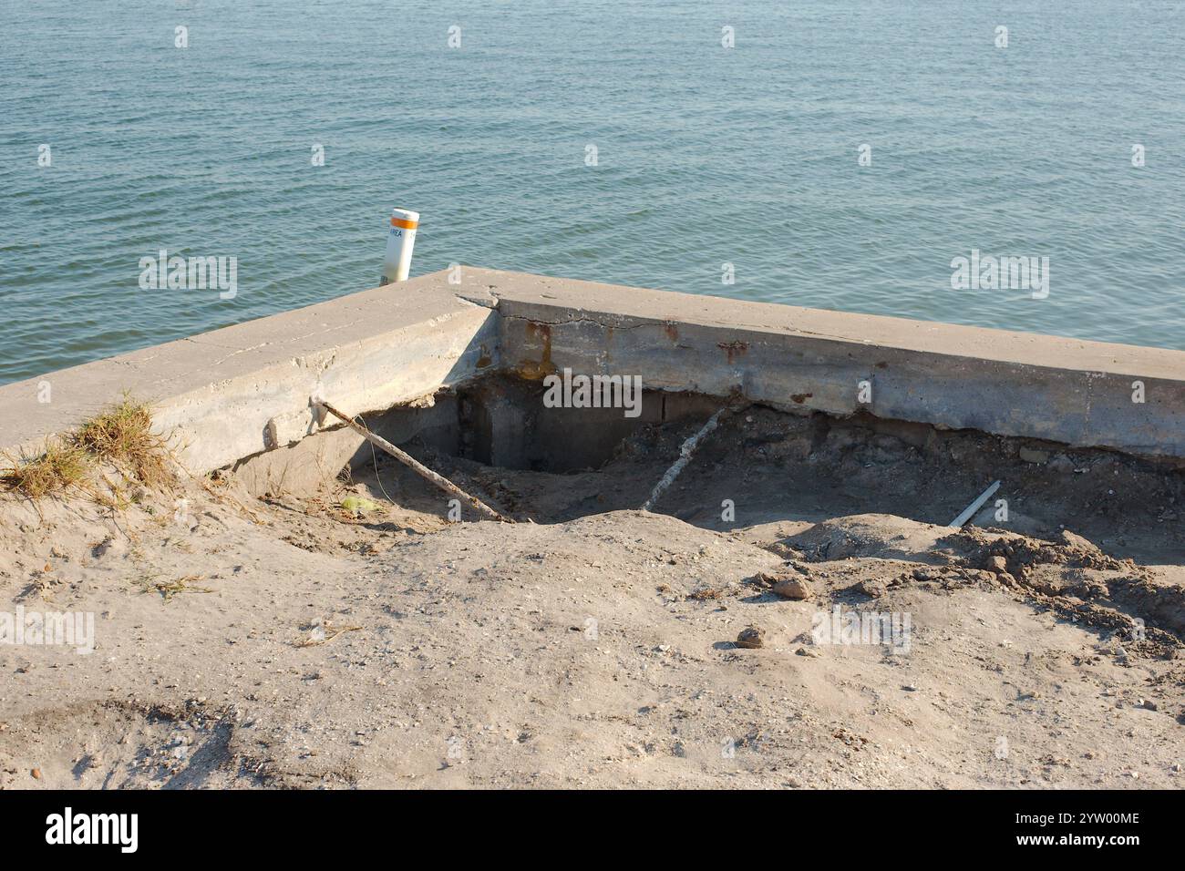 Vue en angle de la digue endommagée par la tempête érodée. Fissures dans les panneaux verticaux et le capuchon de la digue. Calme Blue Bay eau dans le dos par une journée ensoleillée. Blanc et Banque D'Images Vue en angle de la digue endommagée par la tempête érodée. Fissures dans les panneaux verticaux et le capuchon de la digue. Calme Blue Bay eau dans le dos par une journée ensoleillée. Blanc et Banque D'Images