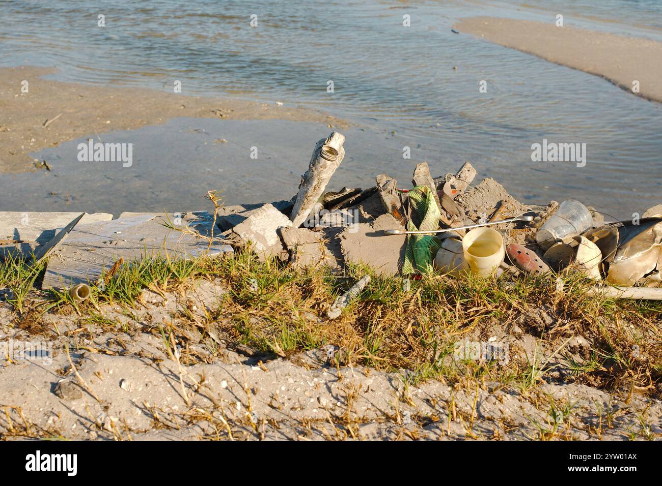 Pile de déchets près du bouchon de la digue en béton. Sable, herbe brune et verte à l'avant et l'eau de baie et barre de sable brun à l'arrière. Petites ondulations dans la baie. Banque D'Images